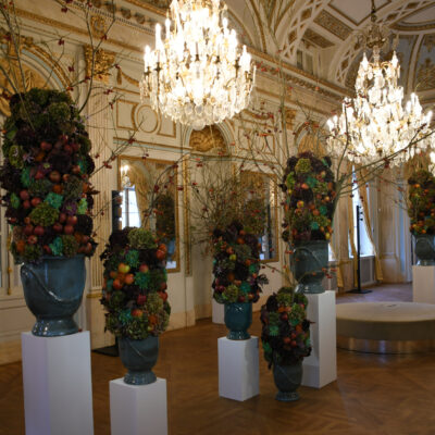 Floraliën Paleis op de Meir - De spiegelzaal Op bezoek in Italië raakt Leopold II betoverd door de balzaal in het paleis van de prinsen Borromeus, gelegen aan het Lago Maggiore. Hij laat in het Antwerpse paleis de eerste twee salons van het appartement van de keizerin ombouwen tot een grote spiegelzaal voor feesten en banketten. De plafonds worden verhoogd en vervangen door een tongewelf. De zaal baadt in lichtblauw en goud, en de plafondversieringen zijn geïnspireerd op de oudheid.   Dat Leopold II de bouwheer was, blijkt duidelijk uit de monogrammen die hij liet aanbrengen. Je herkent ook het stermotief van Congo-Vrijstaat, toen persoonlijk eigendom van de vorst. In 1908 werd het gebied geannexeerd door België als direct gevolg van de internationale kritiek op de wandaden die daar onder zijn regime plaatsvonden. 