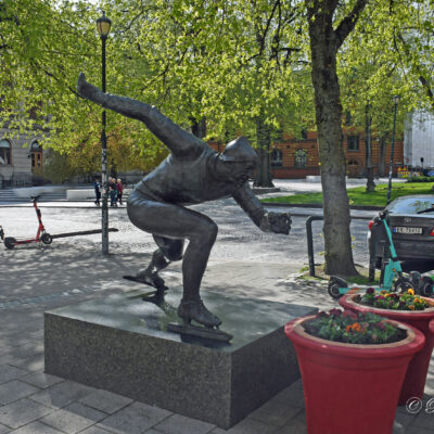 Bronzen beeld van Hjallis Andersen, met armen van de rug. Glijdend op linker schaats. Opschrift: Hjalmar Andersen, Hjallis Achtergrond informatie:  Het beeldhouwwerk, dat ter gelegenheid van het duizendjarig jubileum een geschenk aan de stad was (door Trond Lykke), werd onthuld op de 75ste verjaardag van de schaatskoning. Plannen om het beeld te verplaatsen hebben het niet gehaald, maar een plein in de buurt krijgt zijn naam. Het standbeeld laat Hjallis in actie zien, zoals zoveel mensen hem herinneren. Het is gebaseerd op een foto van de Olympische Spelen in Oslo in 1952, waar Hjallis ook drie gouden medailles won. De armen kenmerkt de laatste meters tijdens de 10.000 meter.